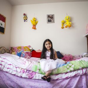 A young Iraqi girl sits inside her bedroom in Portland, OR. Often immigrant children present a mixture of embracing new cultural icons such as Chuck E. Cheese, Tweety Bird and Big Bird.